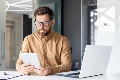 Man in yellow shirt working at desk with white laptop 