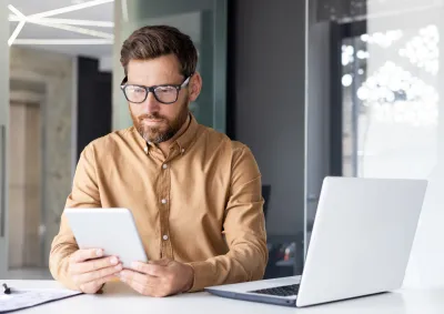 Man in yellow shirt working at desk with white laptop 